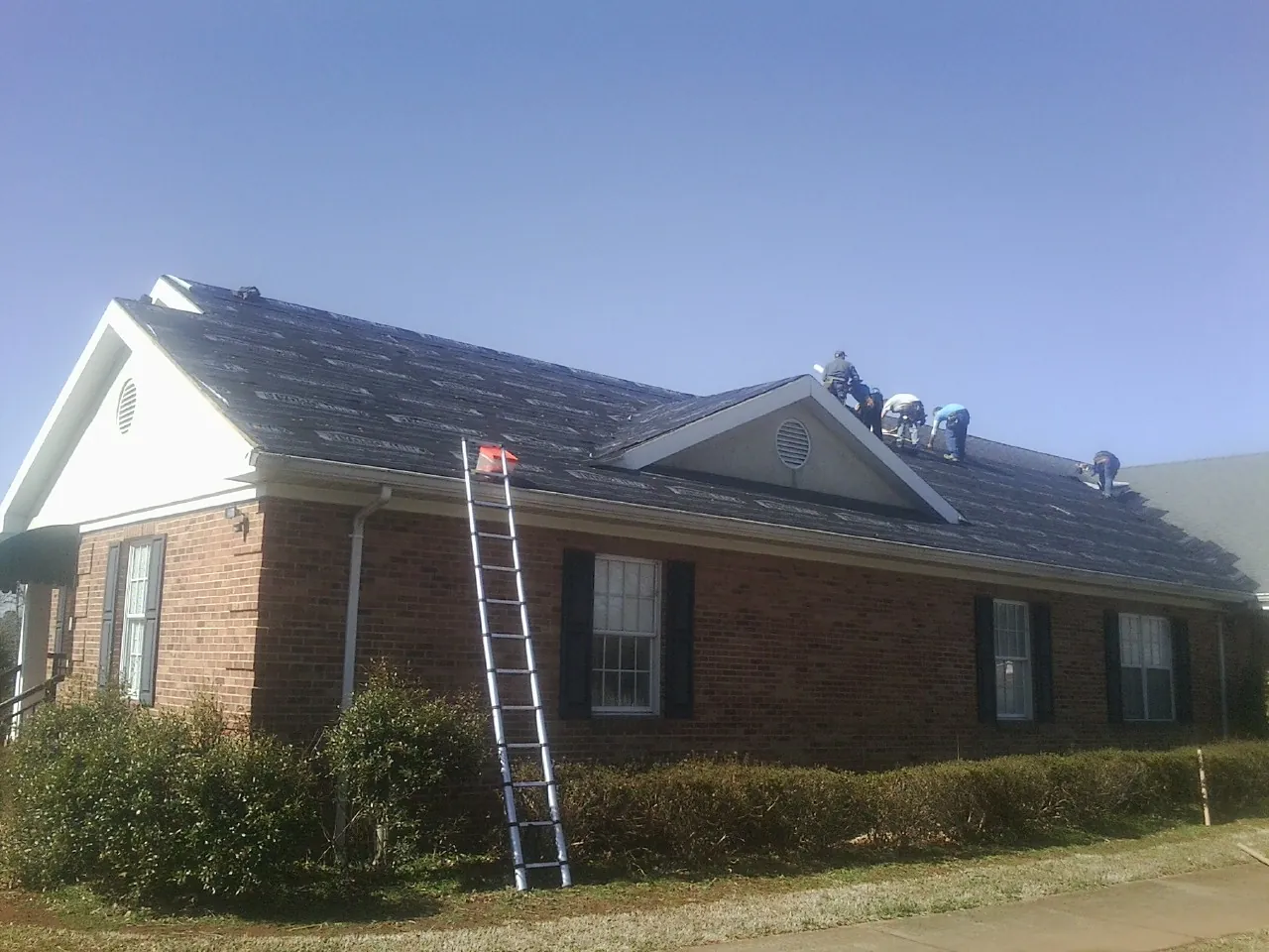 Crew tearing shingles off a brick ranch roof with a ladder set — Emergency Roof Repair work by our crew in Holmdel
