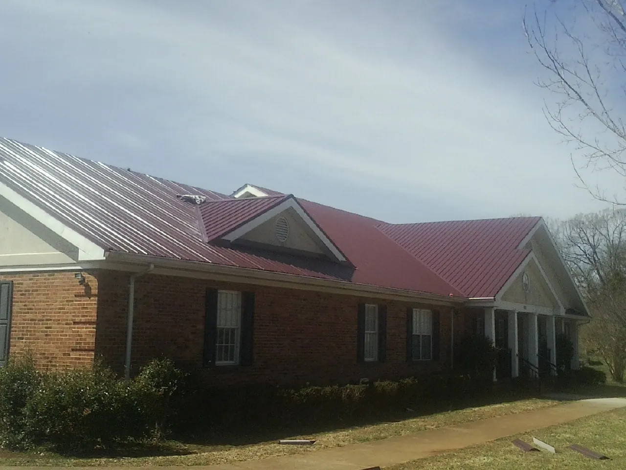 Red metal roof with gabled entries on a long brick building, from a Hail Damage Roof Repair job in Holmdel