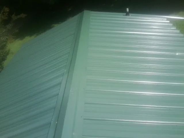 New green metal panels meeting at the ridge of a roof — Flat Roof Repair work by our crew in Holmdel