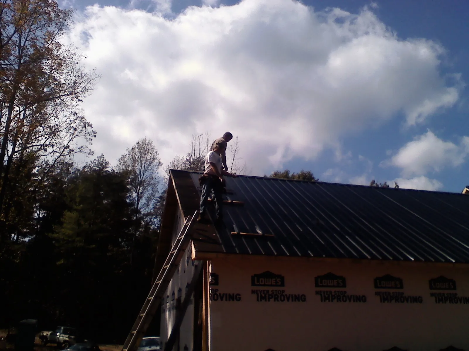 Roofer fastening dark metal panels high against a cloudy sky, from a Roof Inspection job in Holmdel