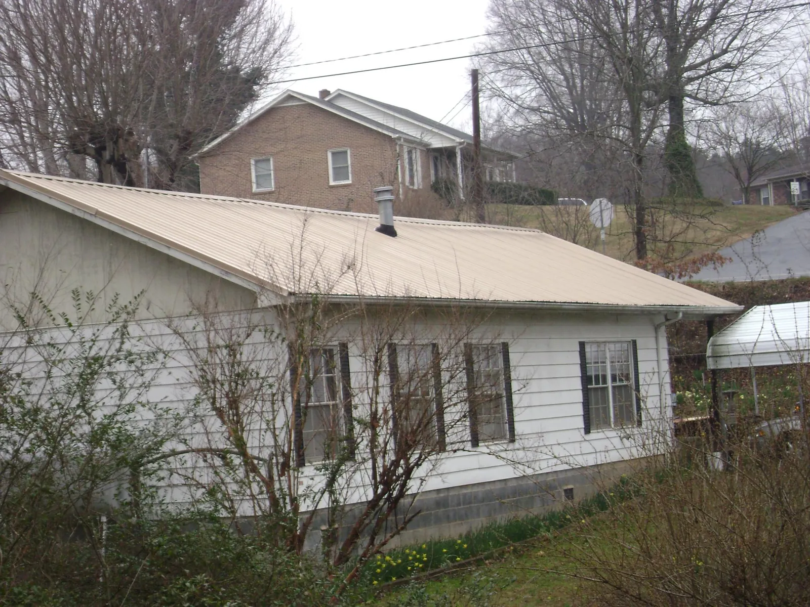 Tan metal roof on a white sided house set into a hillside — Commercial Roofing by Roofing Brothers in Holmdel